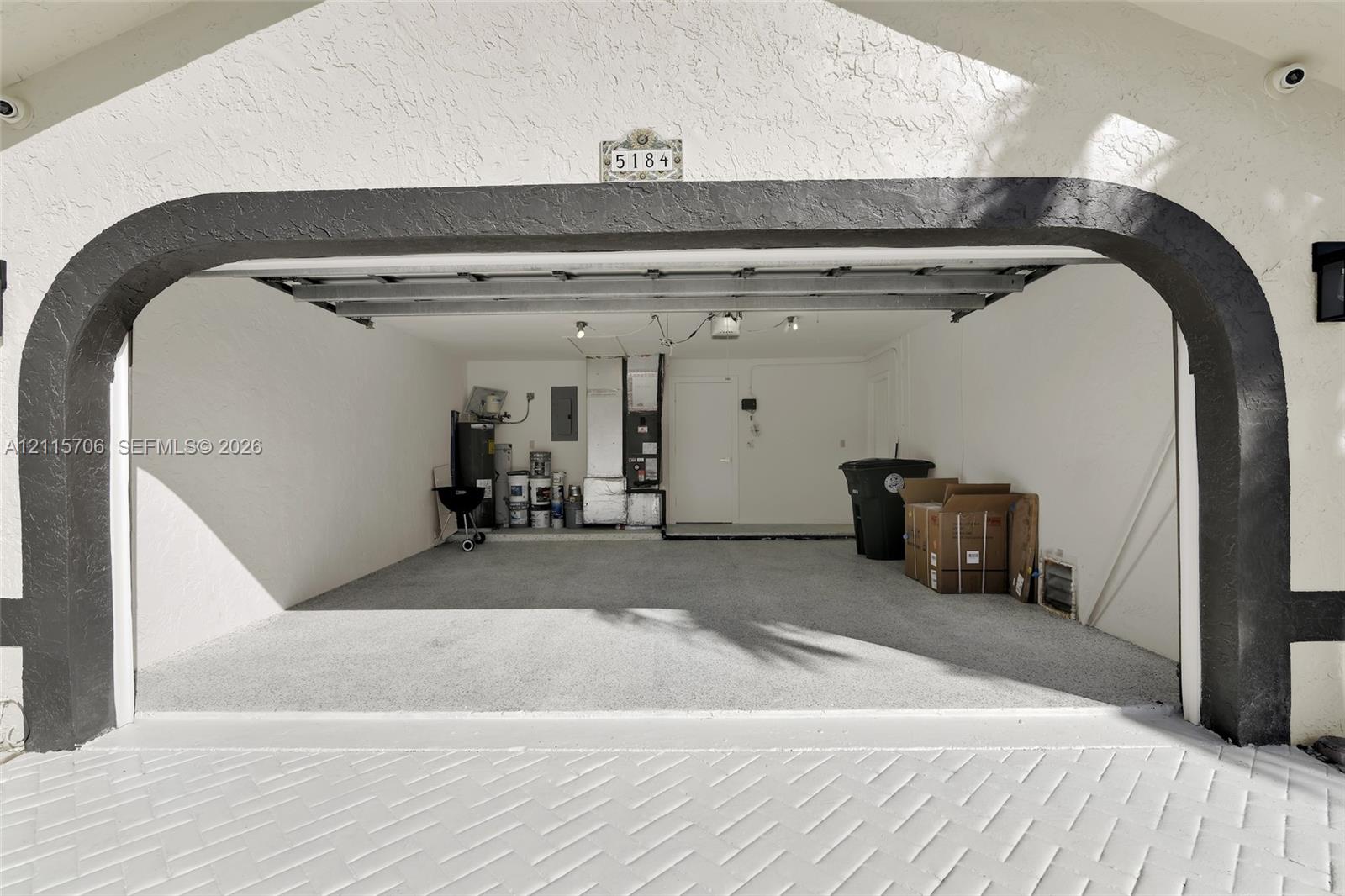 Two-car garage featuring a textured stucco facade, decorative arched entryway, concrete flooring, and ceiling-mounted garage door opener