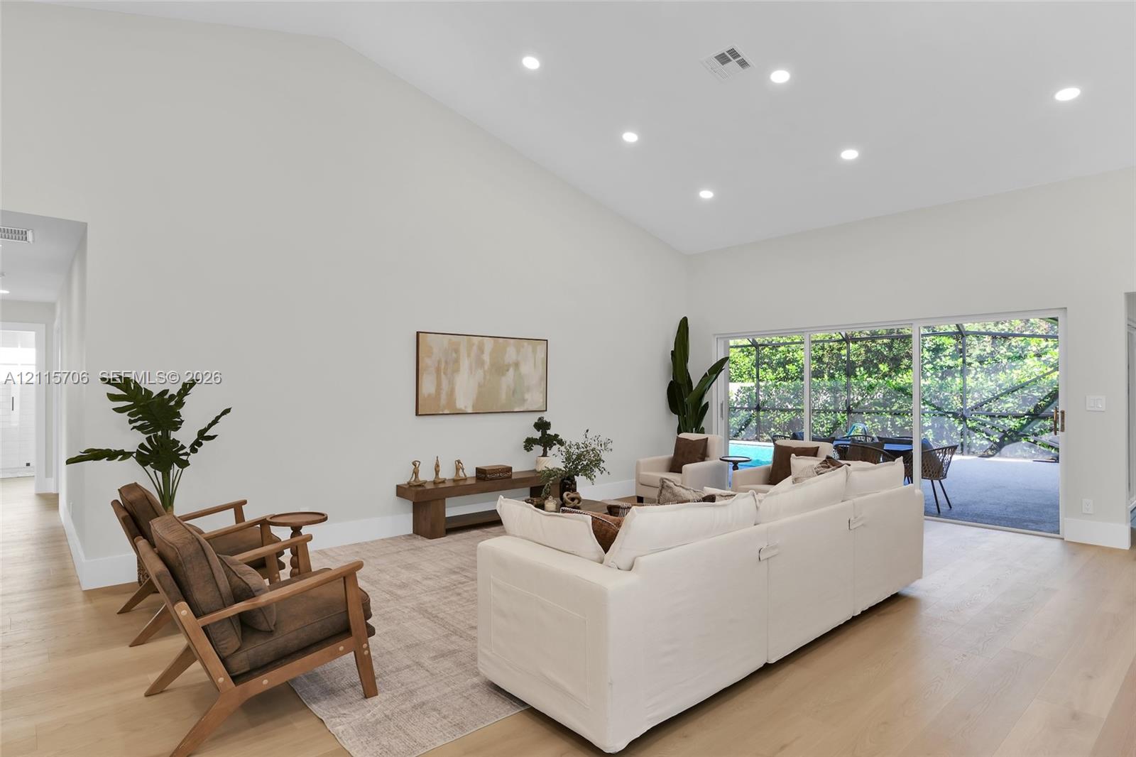 Vaulted ceilings, recessed lighting, wood-finish flooring, and expansive sliding glass doors leading to a screened lanai