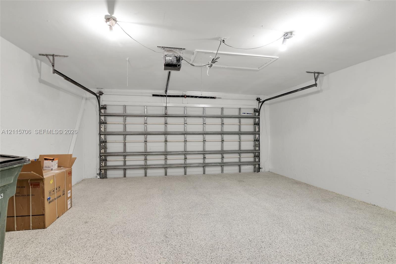 Two-car garage featuring a speckled epoxy-coated floor, high-ceiling configuration, automated door opener, and access panel