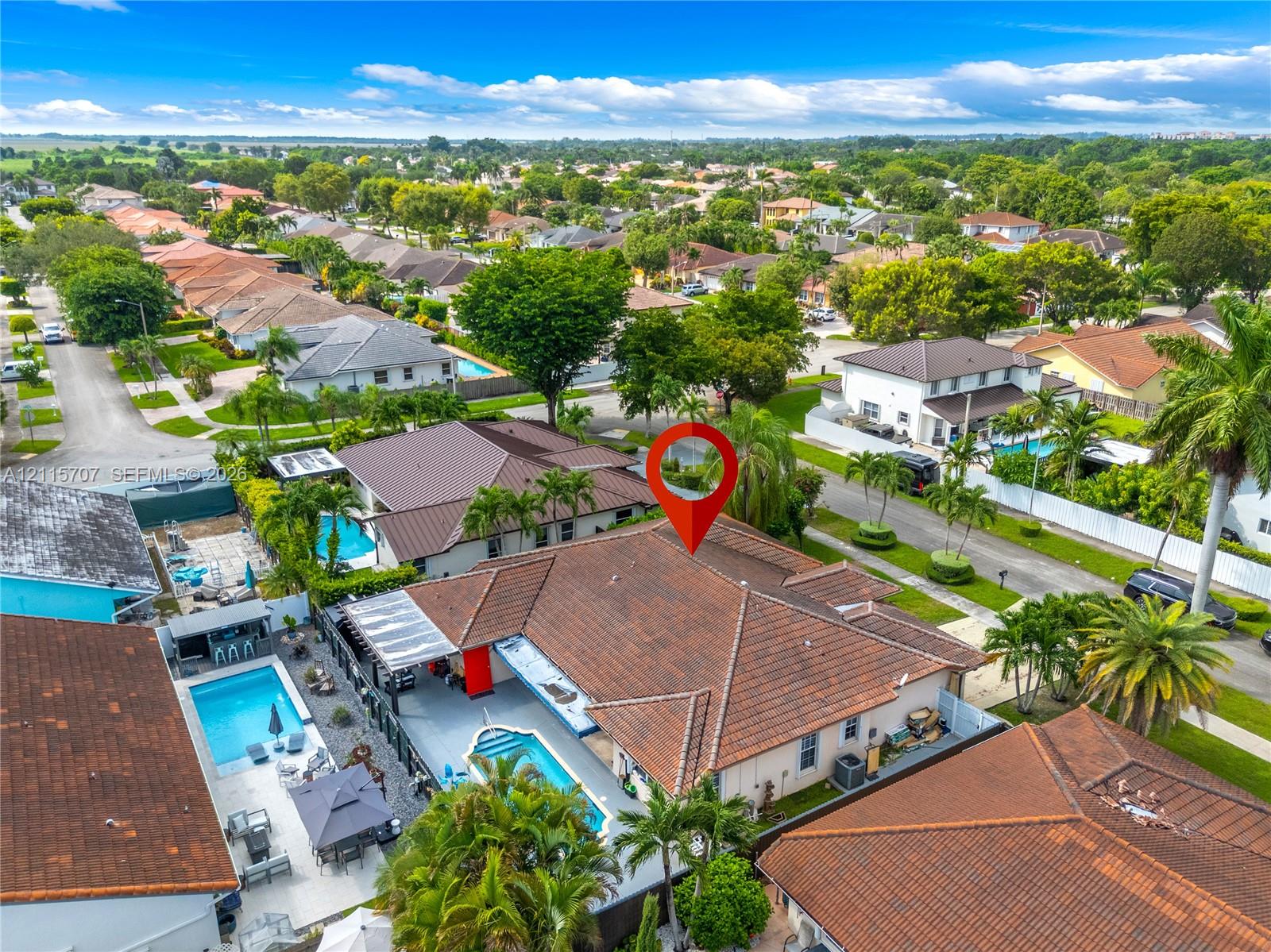 Aerial perspective of a property featuring a tile roof, an in-ground swimming pool, a concrete patio area, and mature landscaping