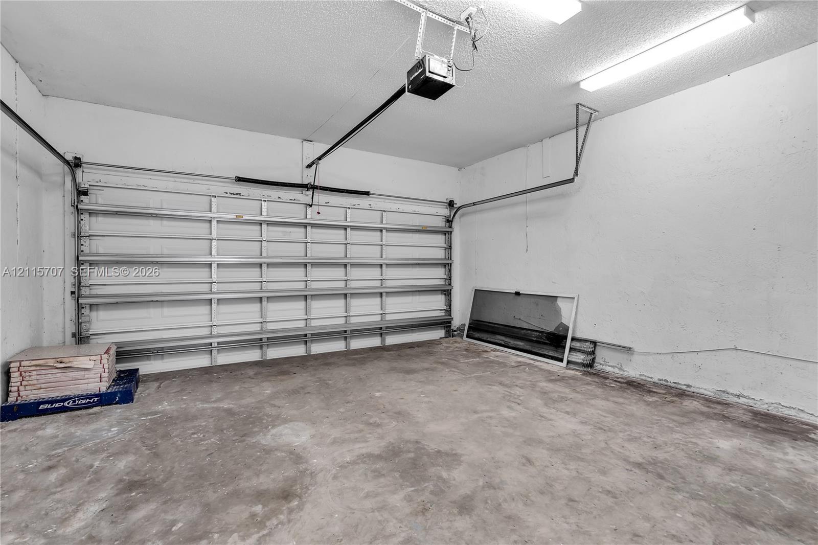 Attached garage featuring concrete flooring, an automated overhead door system, and ceiling-mounted fluorescent lighting