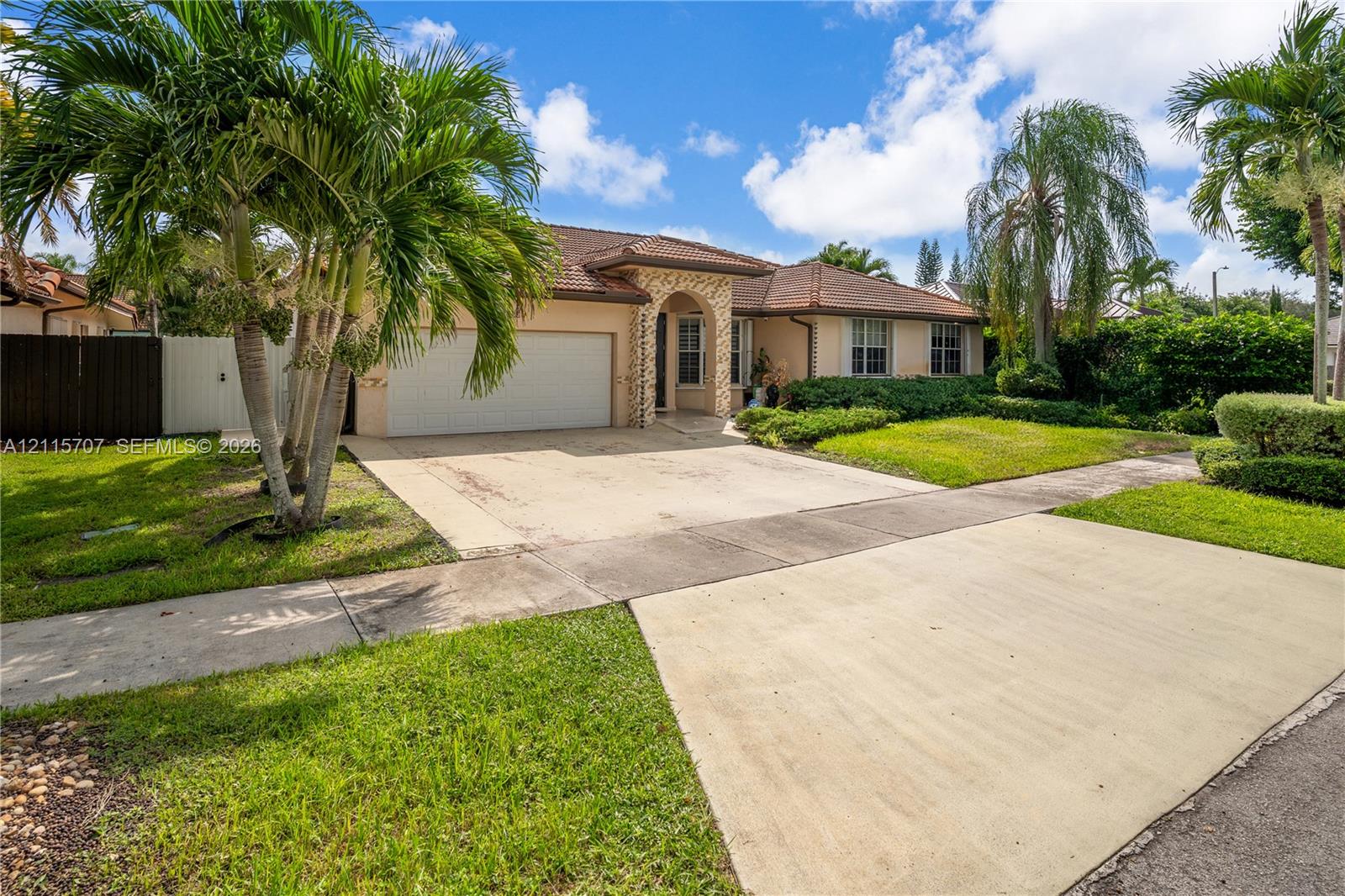Single-story residence featuring a tile roof, masonry exterior, arched entryway, concrete driveway, and mature palm landscaping