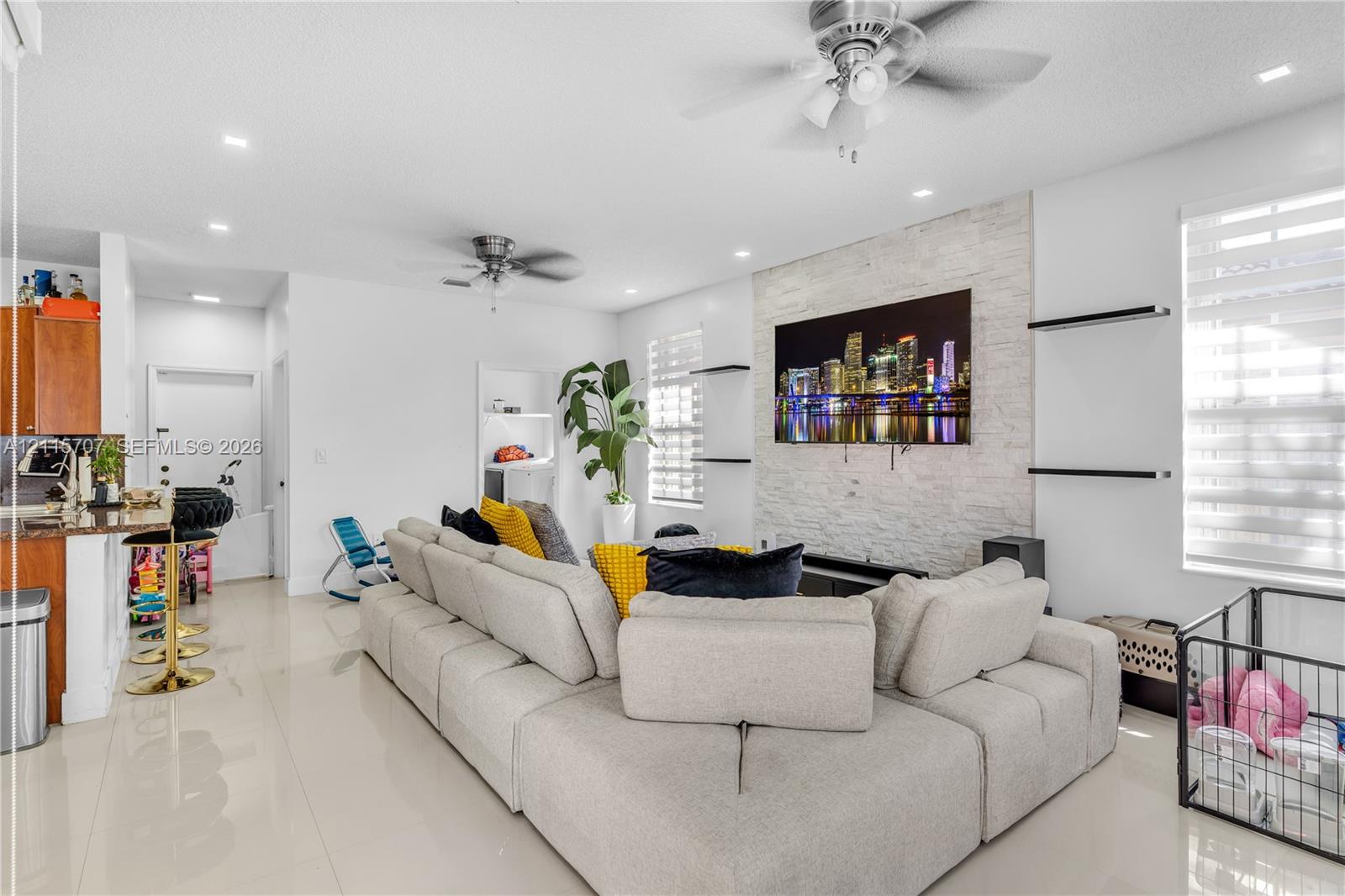 Living area featuring a floor-to-ceiling natural stone veneer accent wall, recessed lighting, ceiling fans, large-format tile flooring, and integrated wall-mounted shelving