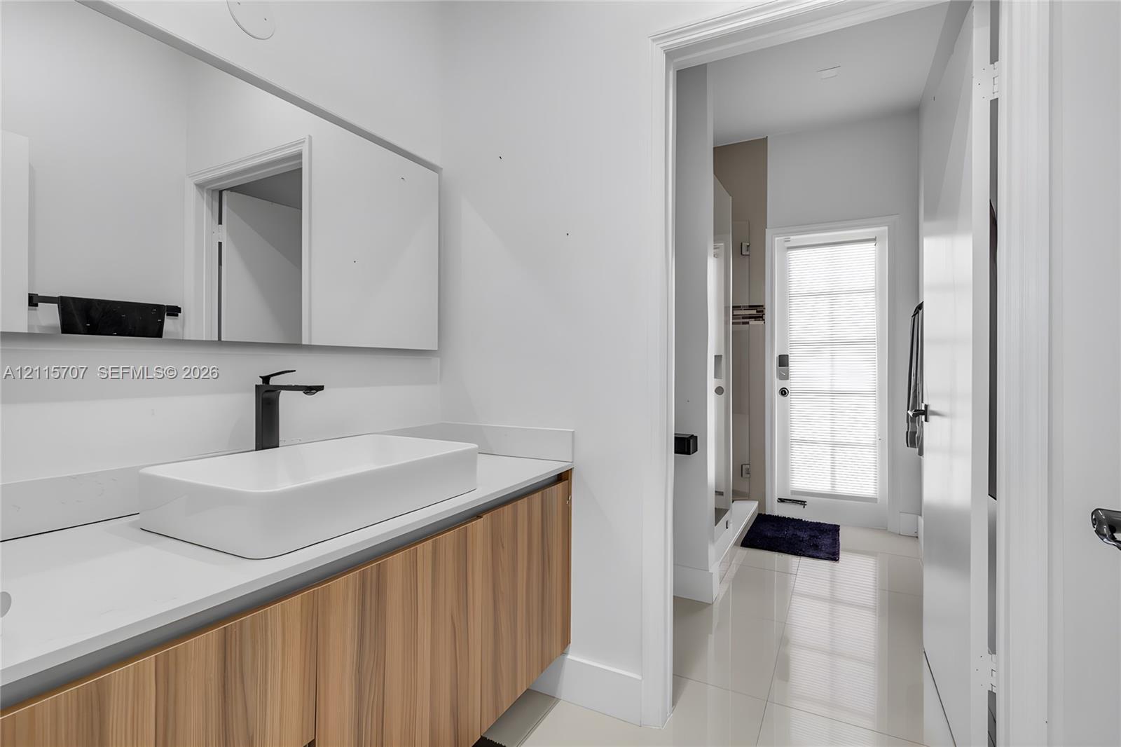 Floating wood-finish vanity with white countertop, rectangular vessel sink, matte black faucet, and large wall-mounted mirror