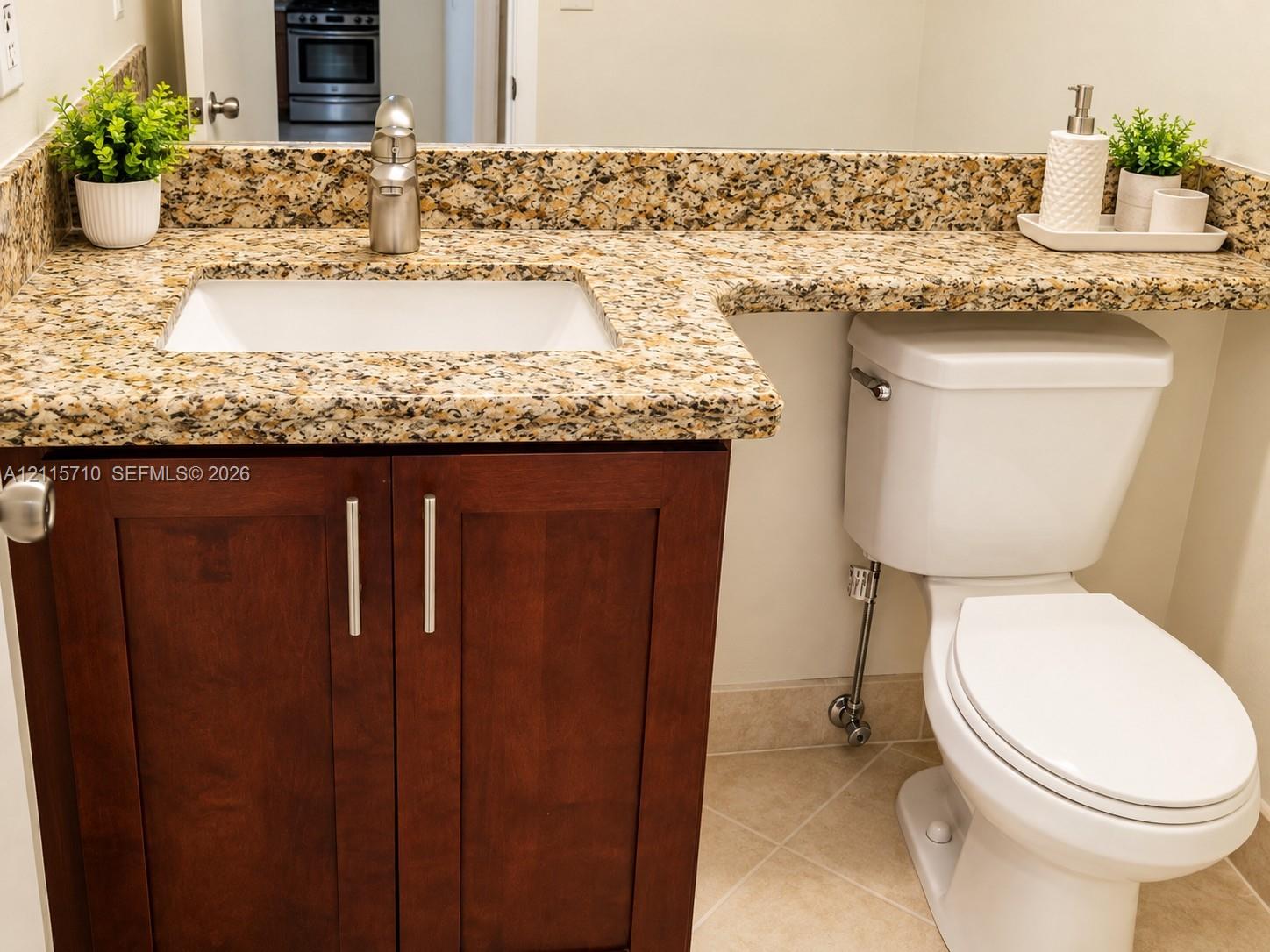 Bathroom vanity featuring a stone countertop with an integrated basin, undermount sink, brushed nickel faucet, and dark wood-finish cabinetry