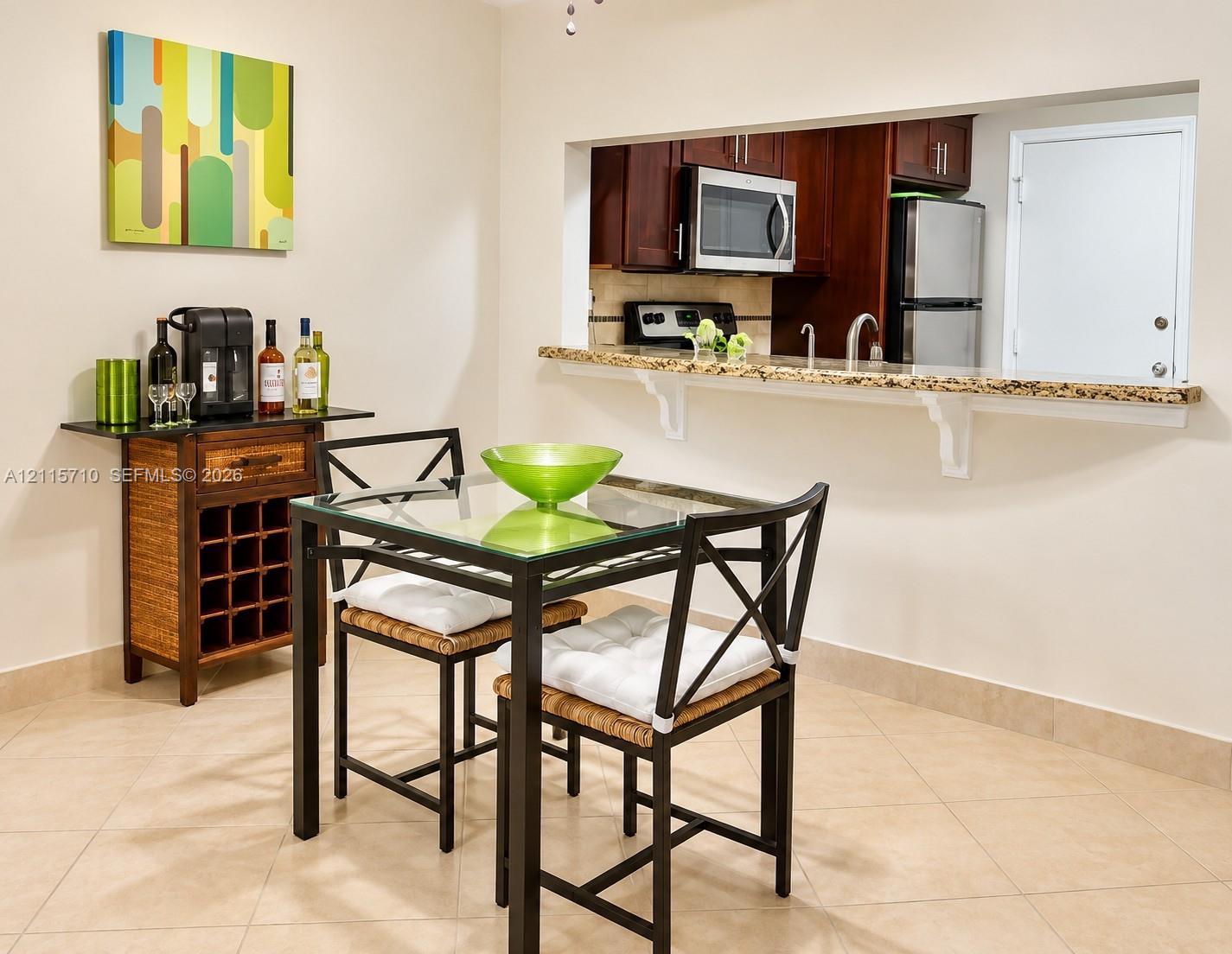 Pass-through window featuring a stone-topped breakfast bar, dark-finish cabinetry, built-in stainless steel microwave, and neutral tile flooring