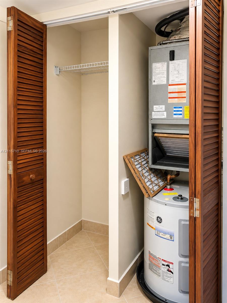 Utility closet featuring wood-finish louvered bi-fold doors, tile flooring, built-in wire shelving, and a dedicated housing for the water heater and HVAC air handler unit