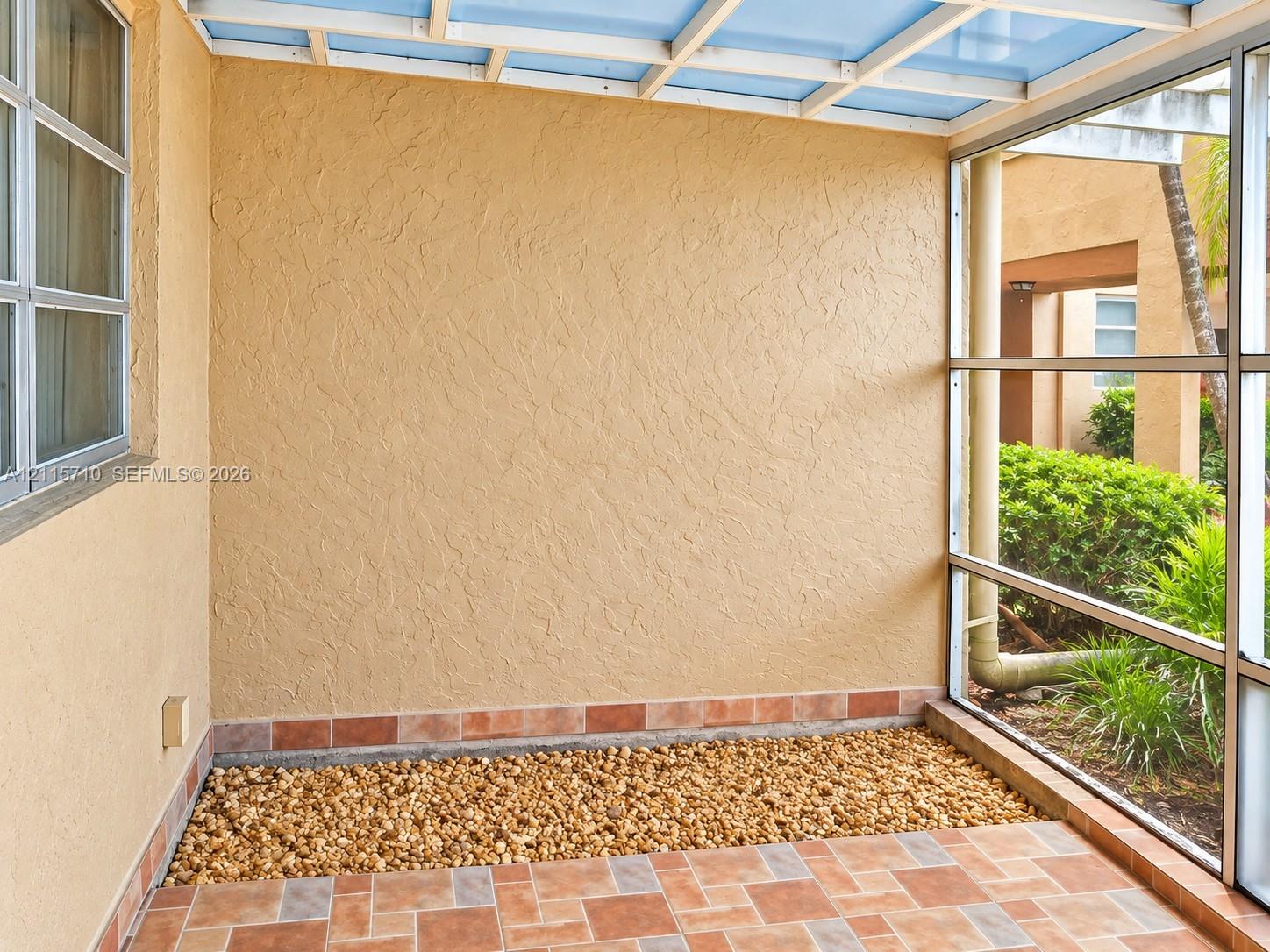 Screened patio featuring a textured stucco finish, multi-tonal ceramic tile flooring, a built-in gravel border, and a translucent roof panel system