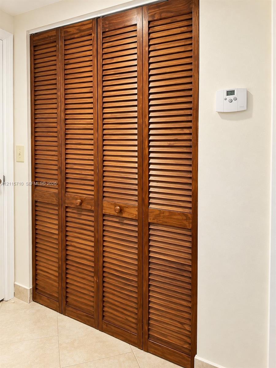 Four-panel closet featuring stained wood louvered doors with circular wood knobs and neutral tile flooring