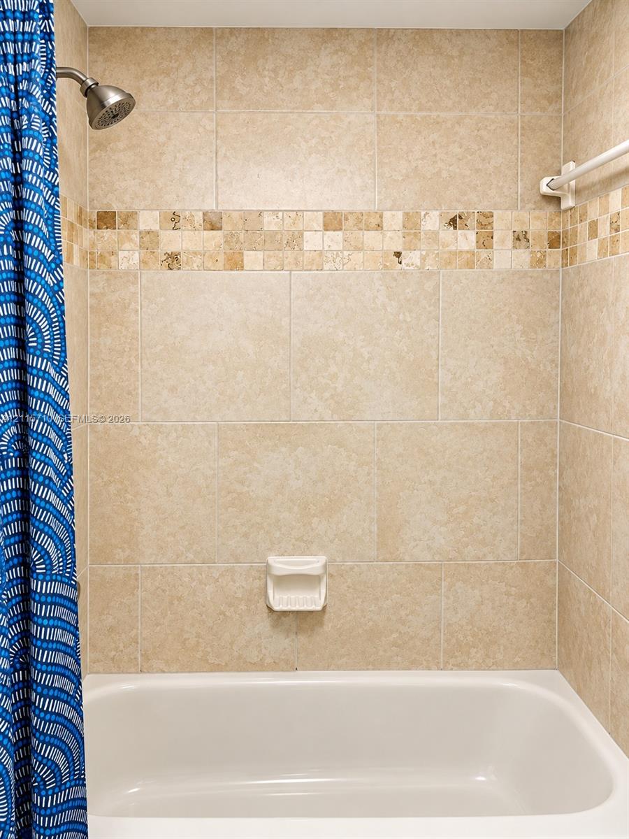 Full-height tile shower surround featuring neutral-toned stone-finish wall tile, an integrated mosaic accent band, a built-in soap dish, and a wall-mounted shower head