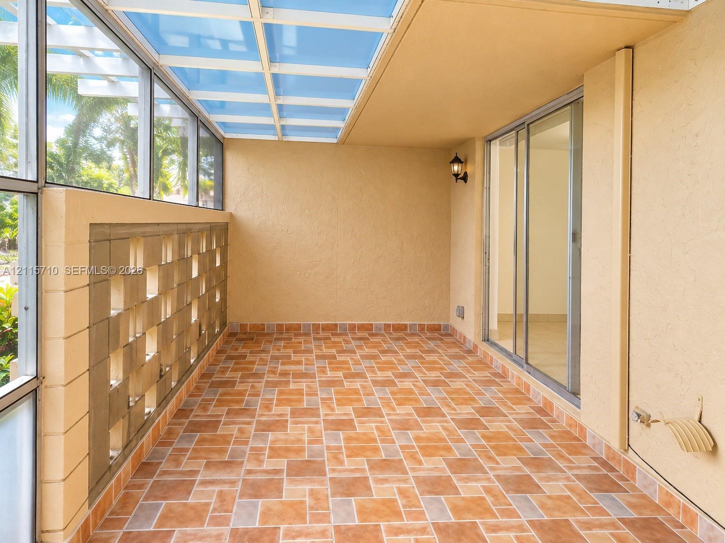 Enclosed patio featuring a translucent roof panel, decorative concrete block wall, patterned ceramic tile flooring, and sliding glass door entry