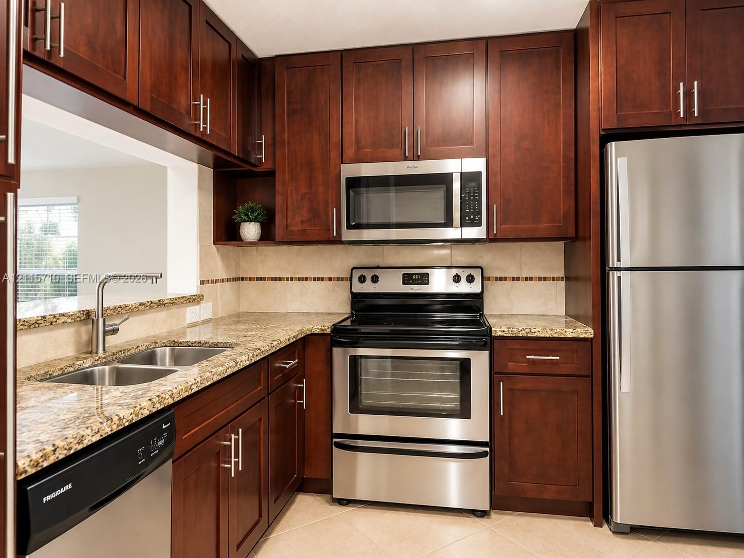 Kitchen featuring dark wood cabinetry, stone-finish countertops, stainless steel appliances, and a double-basin under-mount sink