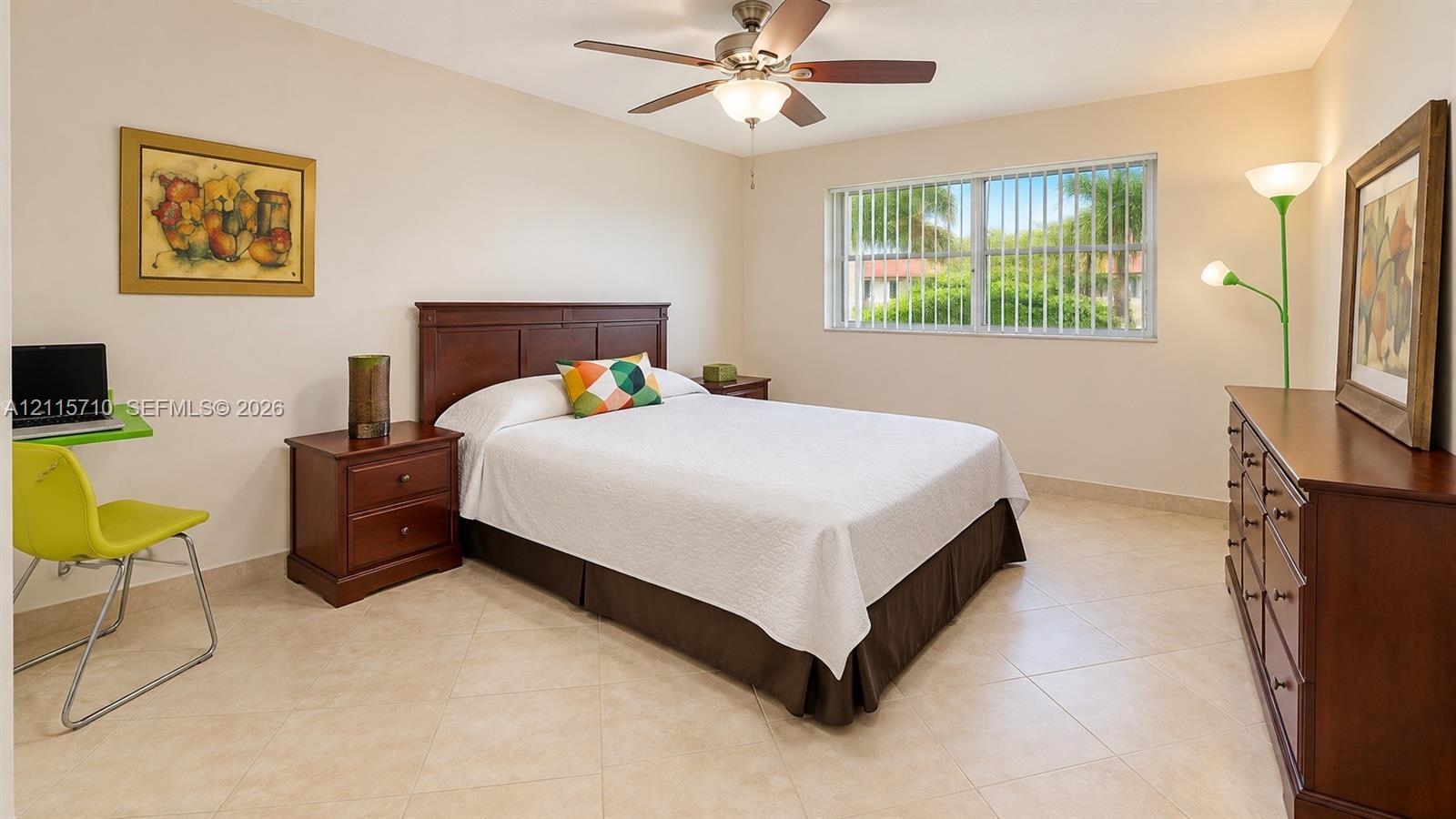 Spacious room featuring neutral tile flooring, a horizontal sliding window with integrated security bars, and a multi-blade ceiling fan with an integrated light fixture