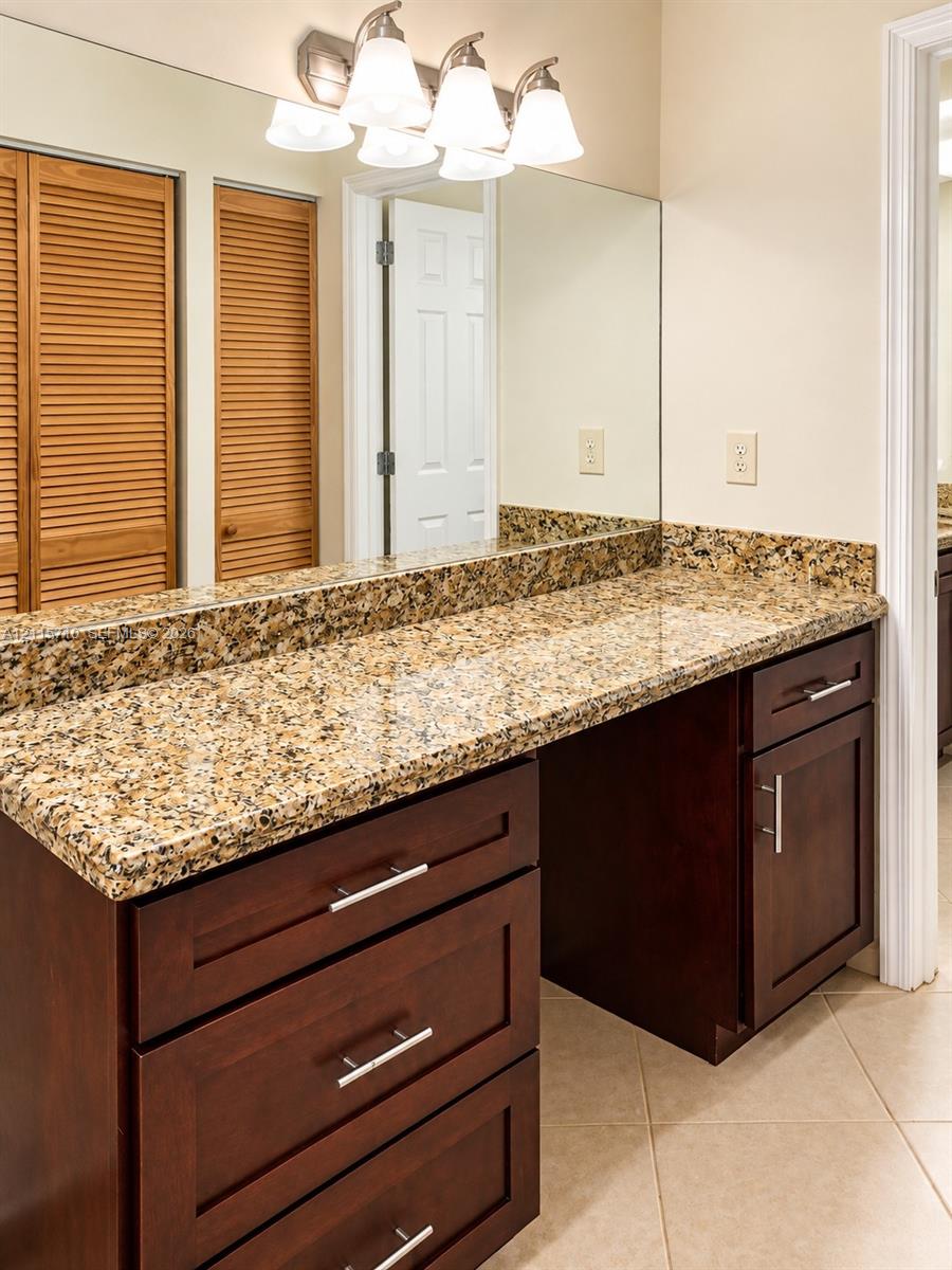 Vanity featuring dark wood-finish cabinetry, stone countertop, full-width mirror, brushed metal hardware, and multi-bulb light fixture