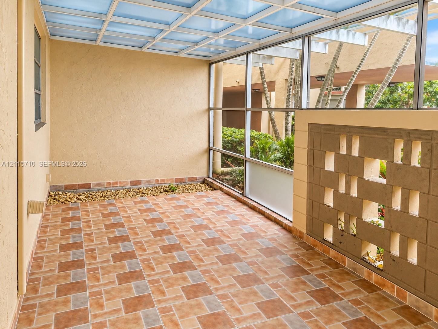 Screened-in patio featuring patterned tile flooring, a translucent roof structure, decorative masonry screen wall, and a stone-lined planter border