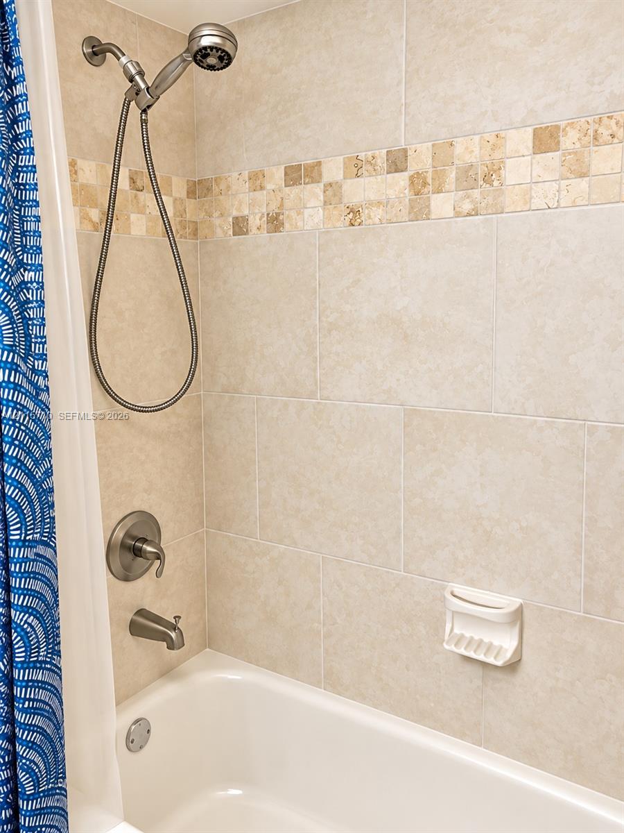 Shower and tub combination featuring large-format neutral tile surround, integrated stone mosaic accent border, satin nickel plumbing fixtures, and a built-in soap dish