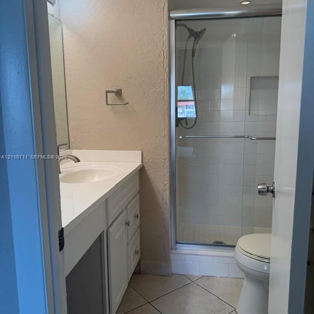 Bathroom featuring a white vanity cabinet, solid-surface countertop with an integrated basin, tile flooring, and a glass-enclosed shower with subway tile surround and a recessed storage niche