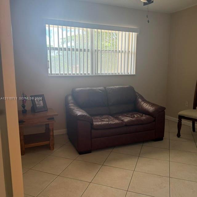 Neutral-toned interior room featuring tile flooring, a large window with vertical blinds, and an attached ceiling fan