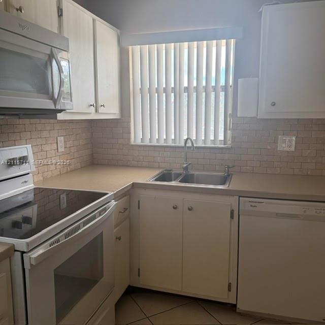 Kitchen featuring light-toned cabinetry, a textured brick-pattern backsplash, an integrated microwave, a double-basin stainless steel sink, and tile flooring