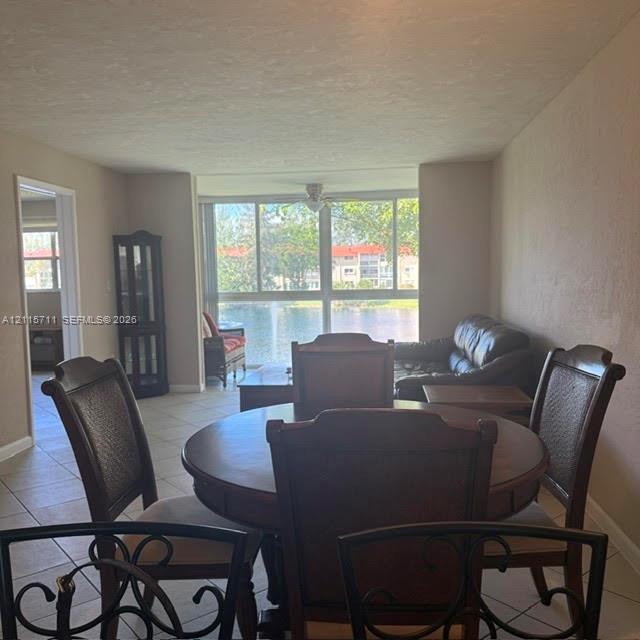 Neutral-toned interior featuring ceramic tile flooring, a ceiling fan, and large floor-to-ceiling windows with water scenery