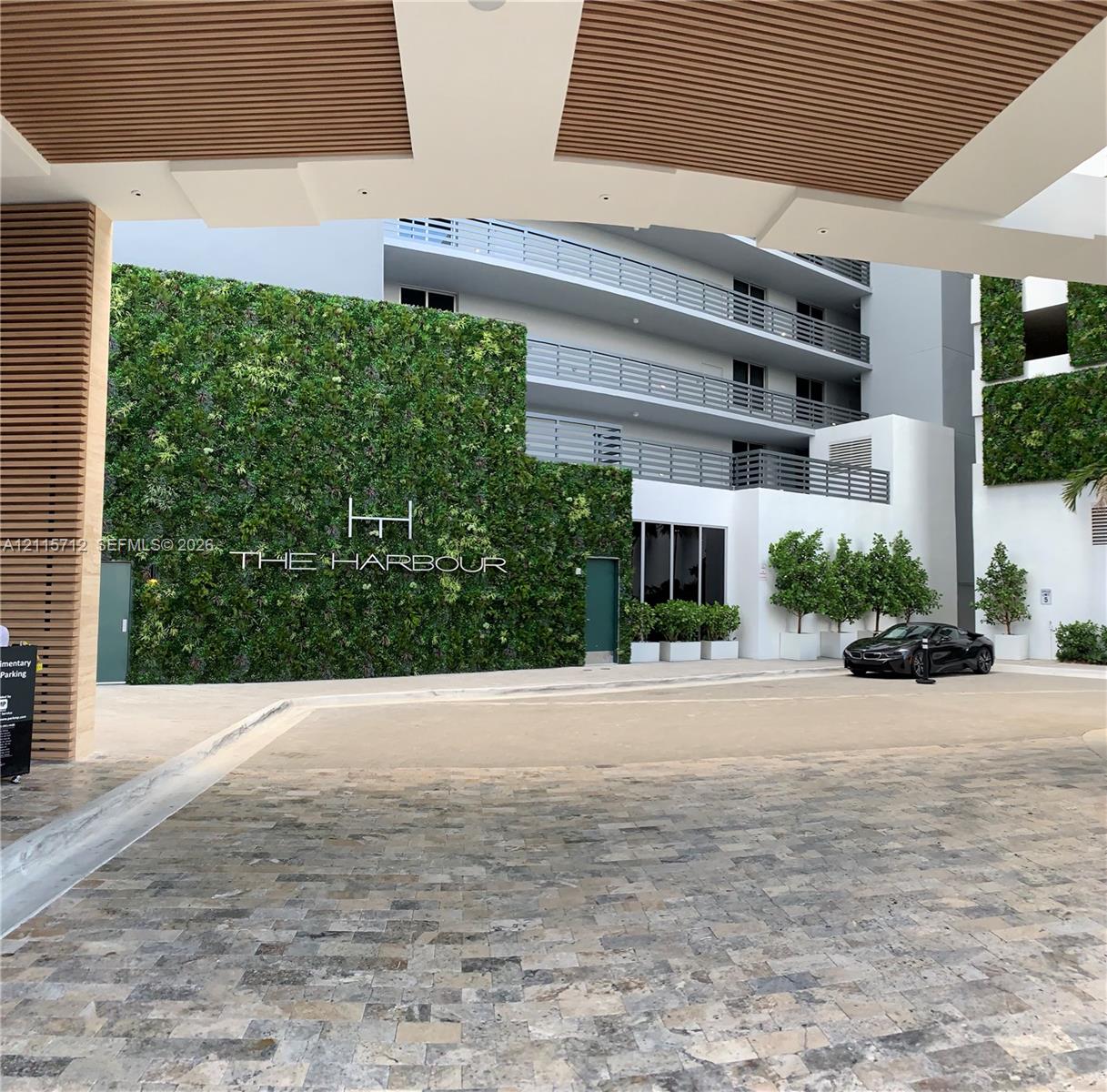 Covered motor court featuring natural stone paving, architectural wood-slat ceiling detailing, a multi-story living green wall, and tiered balconies with horizontal railings