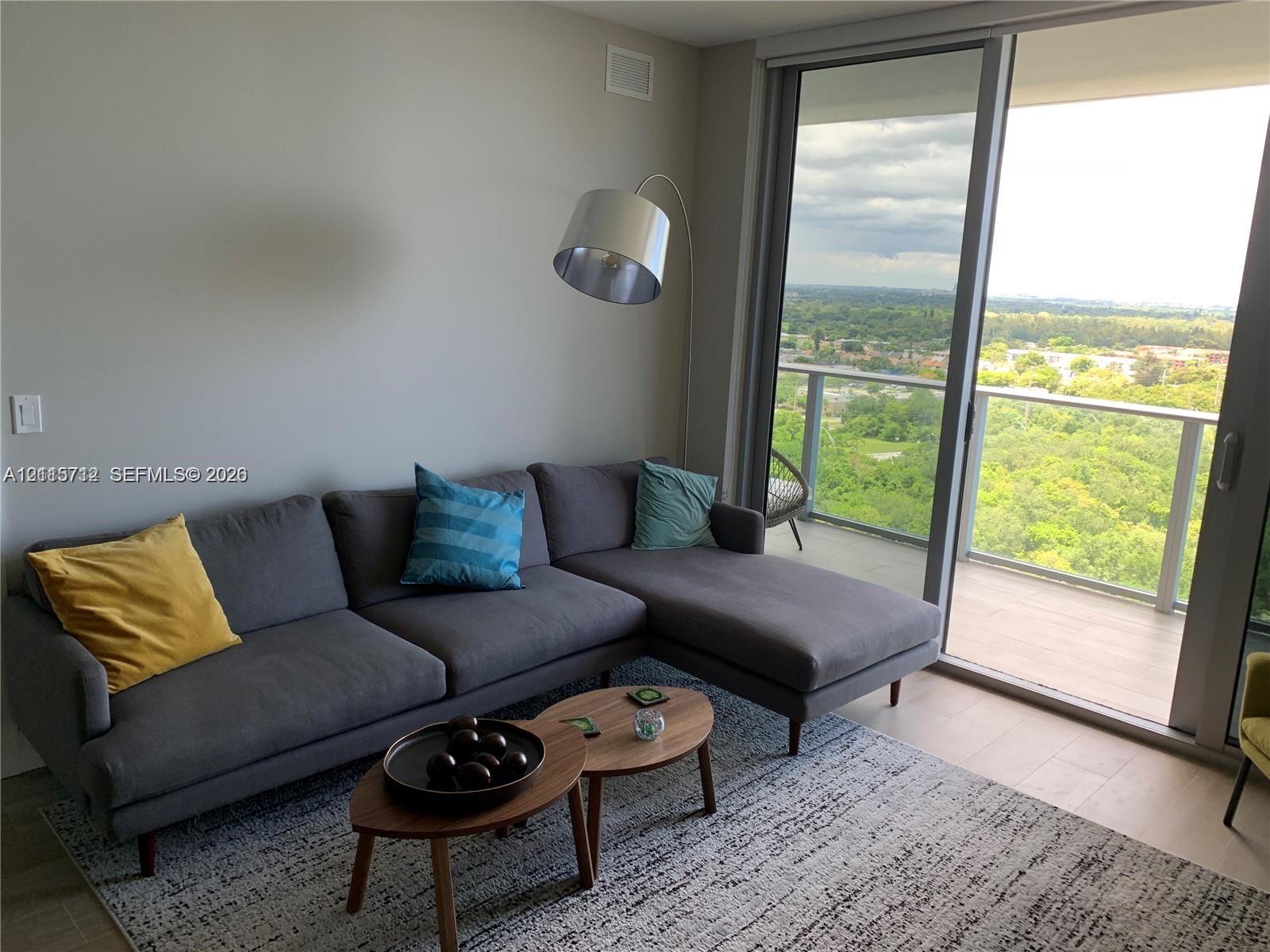 Floor-to-ceiling sliding glass door, private balcony with metal railing, and wood-finish flooring