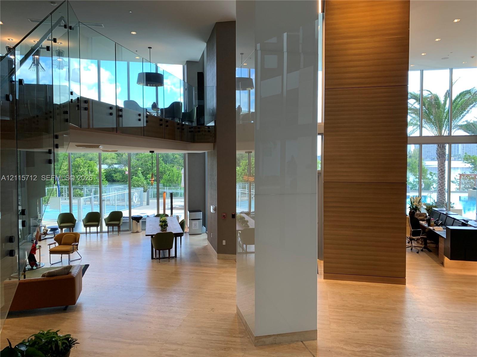 Double-height interior featuring floor-to-ceiling glass walls, glass-panel staircase railing, wood-finish flooring, and wood-paneled accent wall
