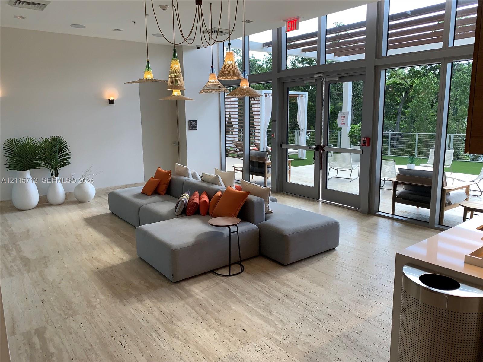 Open-concept space featuring stone tile flooring, floor-to-ceiling glass windows, an integrated pergola structure, and multi-pendant lighting fixtures