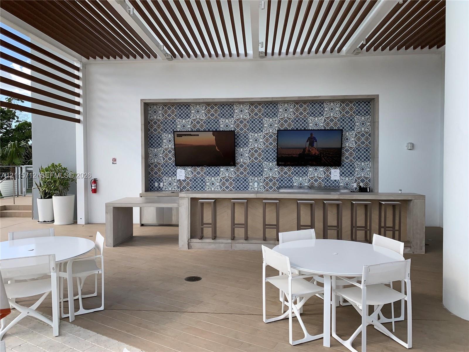 Outdoor covered patio featuring a slatted pergola ceiling, concrete bar with patterned tile backsplash, and wood-finish flooring