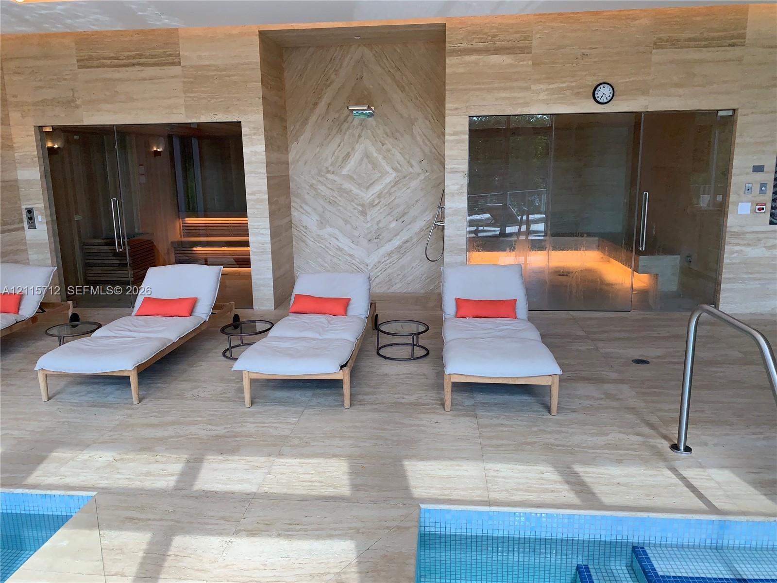 Spa area featuring full-height natural stone wall cladding, floor-to-ceiling glass-enclosed sauna, steam room, and built-in tiled plunge pool with integrated metal handrail