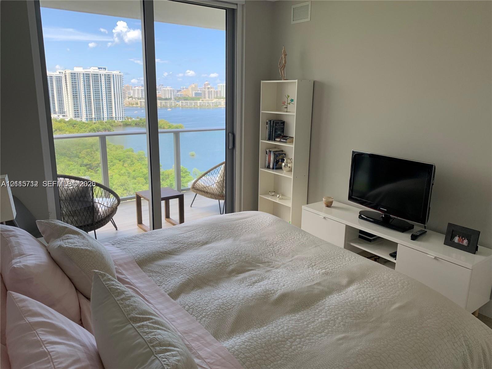 Floor-to-ceiling glass sliding doors opening to a private balcony with metal railing, floor-to-ceiling windows, and expansive waterfront scenery