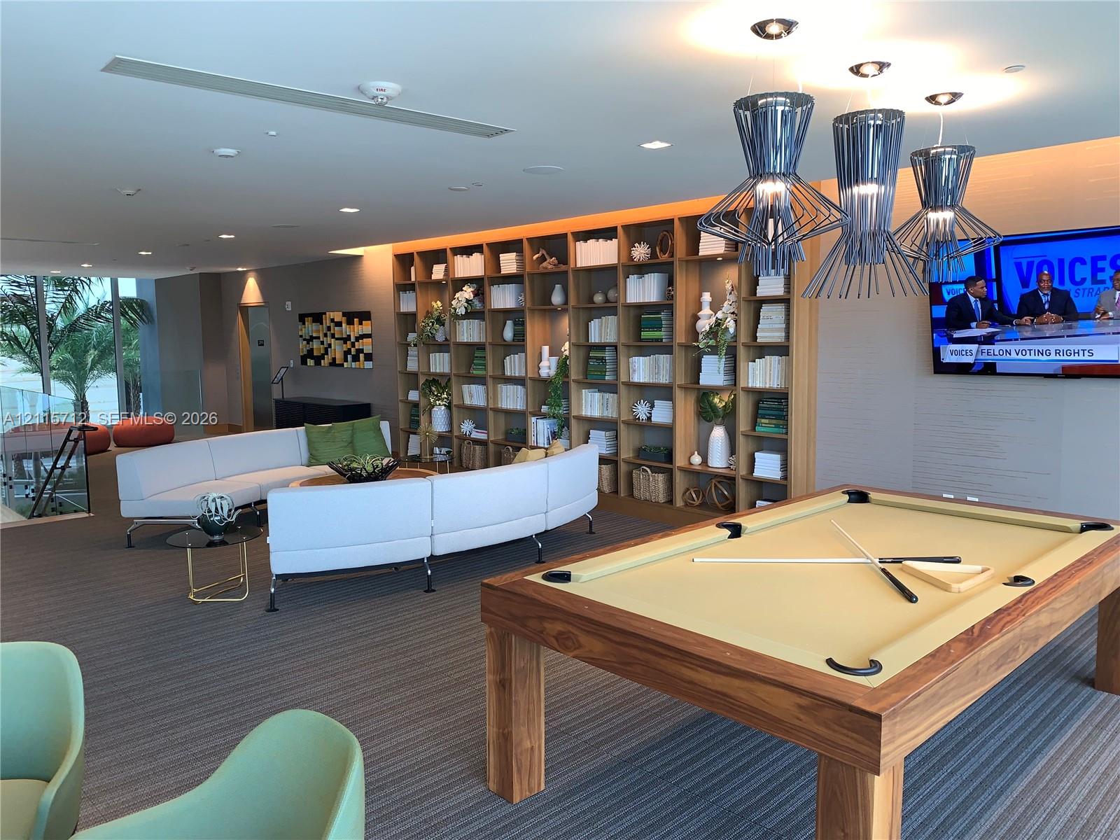 Floor-to-ceiling built-in wooden shelving, recessed ceiling lighting, textured wall-to-wall carpeting, and metal geometric pendant light fixtures