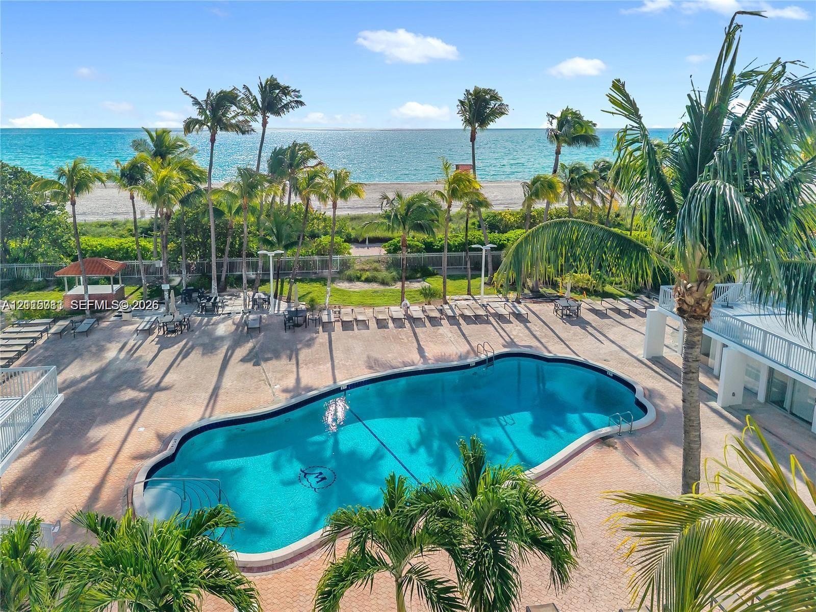 Swimming pool with a stone paver deck, palm trees, and direct ocean backdrop