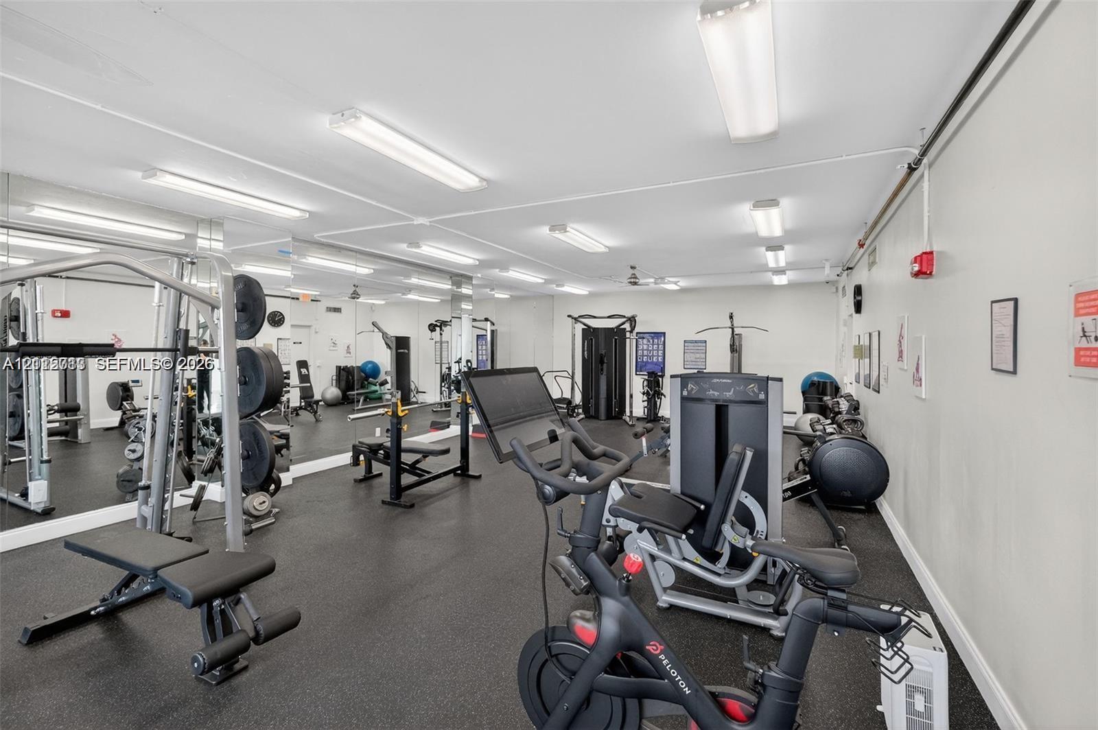 Fitness room featuring rubber flooring, full-length wall mirrors, and overhead fluorescent lighting