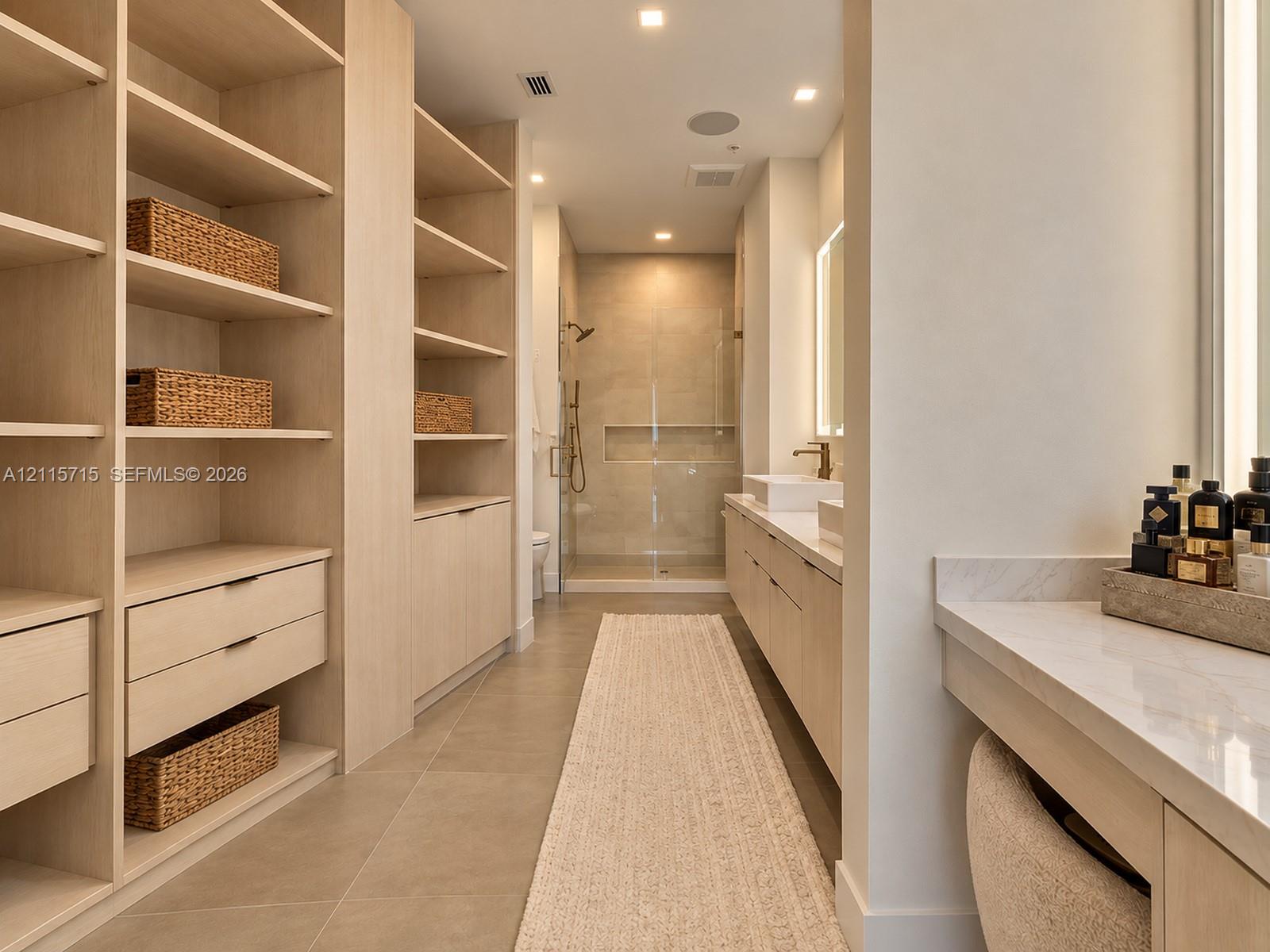 Custom built-in wood cabinetry, expansive walk-in storage, dual-sink vanity with stone countertop, frameless glass shower enclosure, and recessed lighting