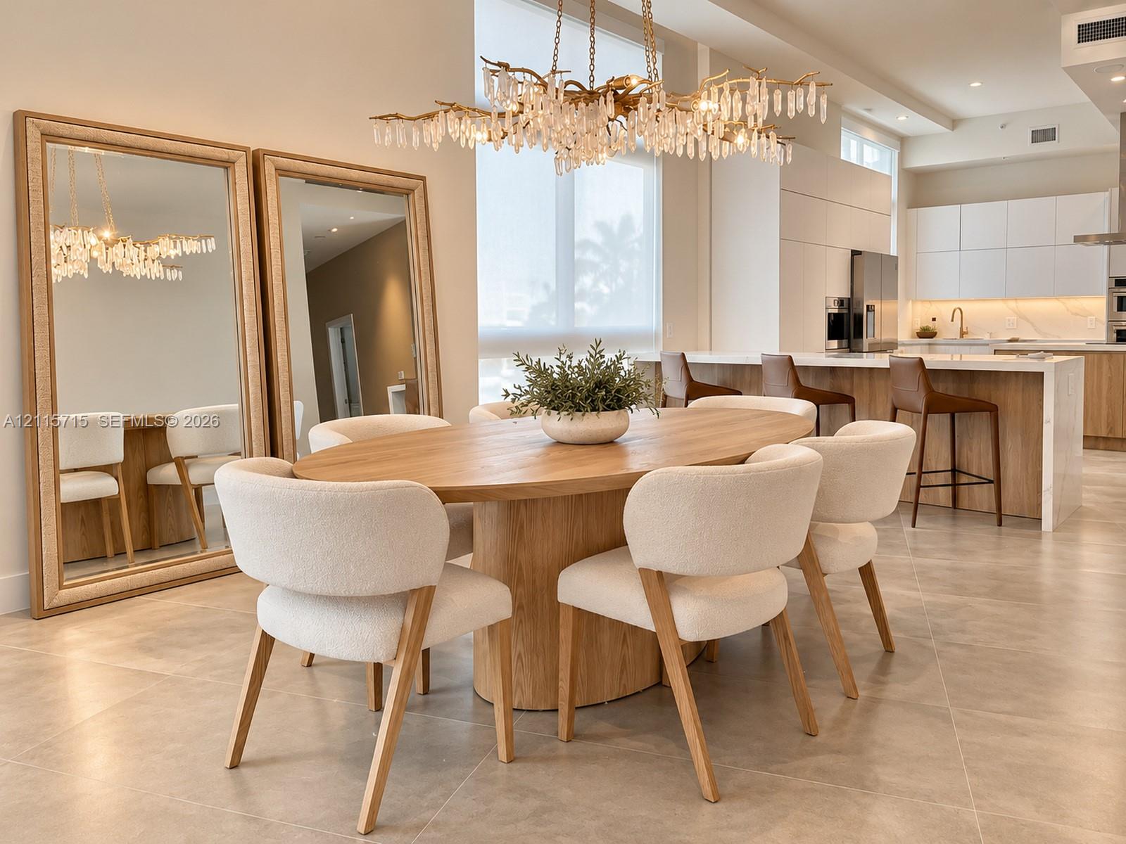 Open-concept interior featuring large-format tile flooring, a multi-tiered crystal statement chandelier, and a kitchen equipped with handleless flat-panel cabinetry and a waterfall-edge island