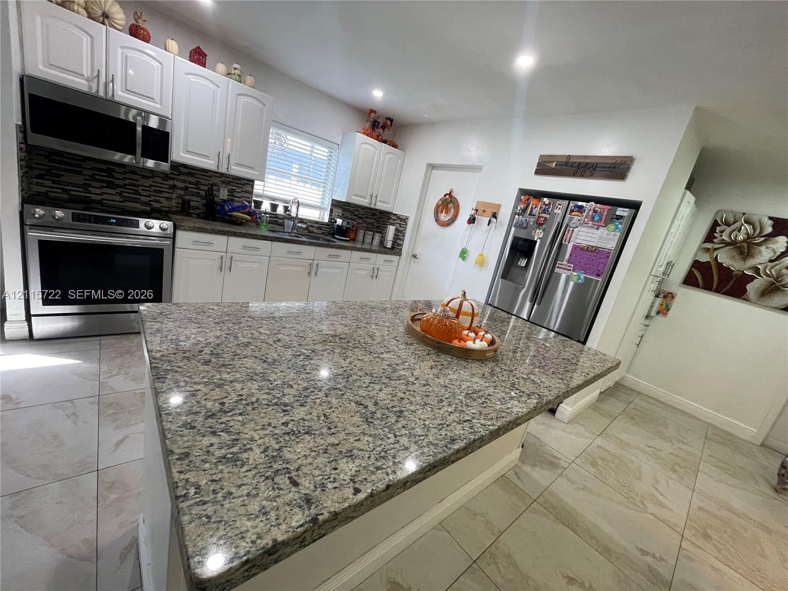 Kitchen featuring a center island with stone countertop, white shaker-style cabinetry, stainless steel appliances, and tile flooring