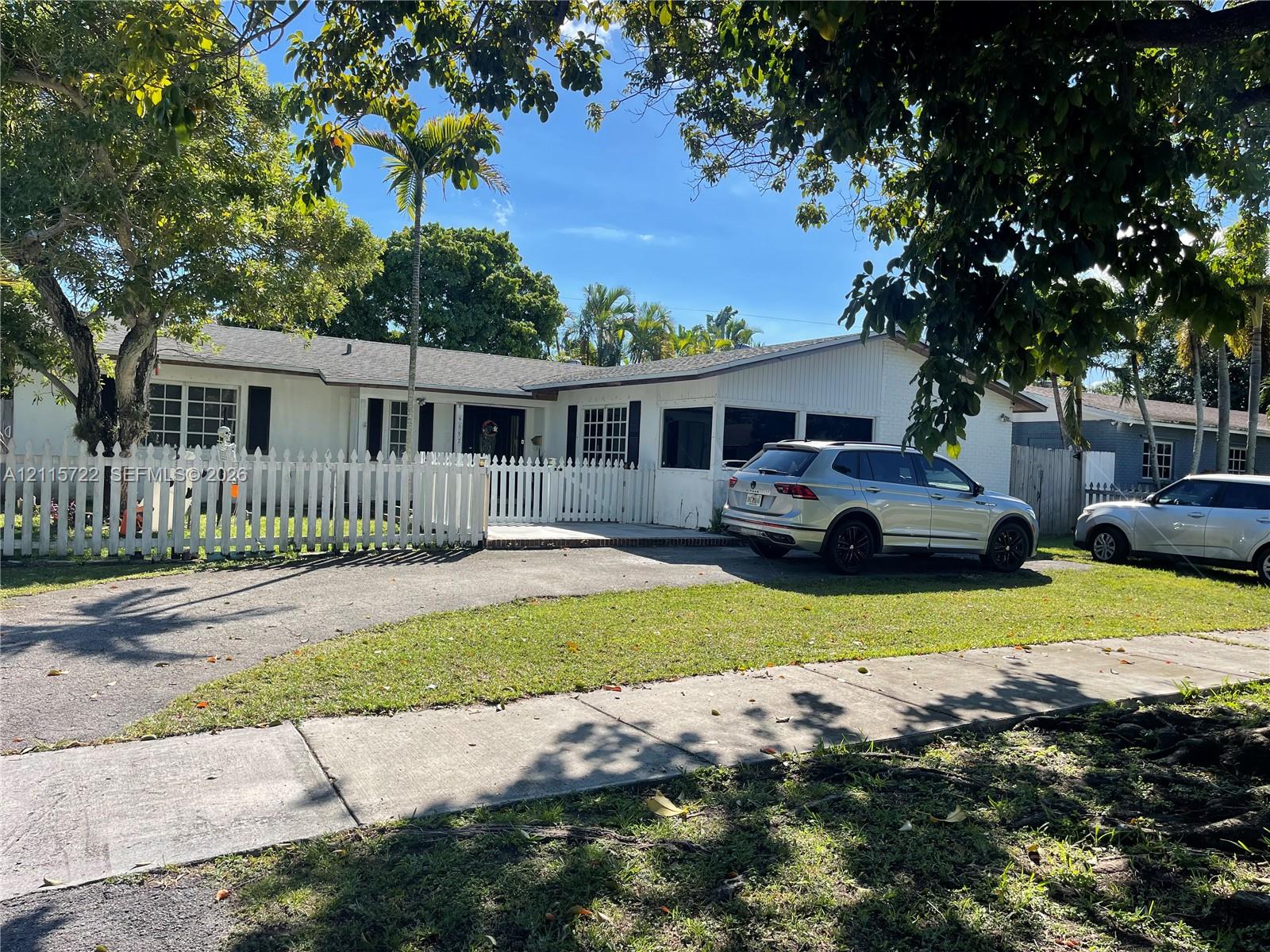 Single-story exterior featuring white vertical siding, a picket fence perimeter, asphalt-paved driveway, and a screened-in porch