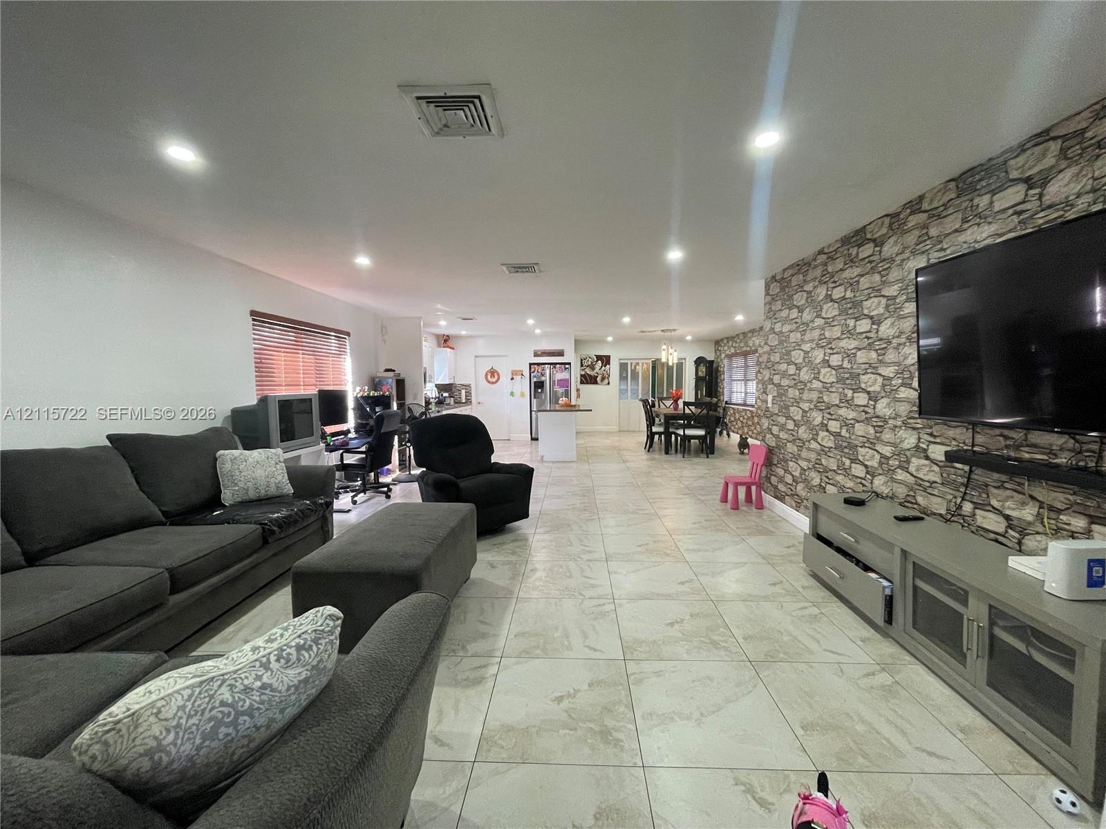 Open-concept interior featuring large-format ceramic tile flooring, stone-veneer accent wall, and recessed lighting