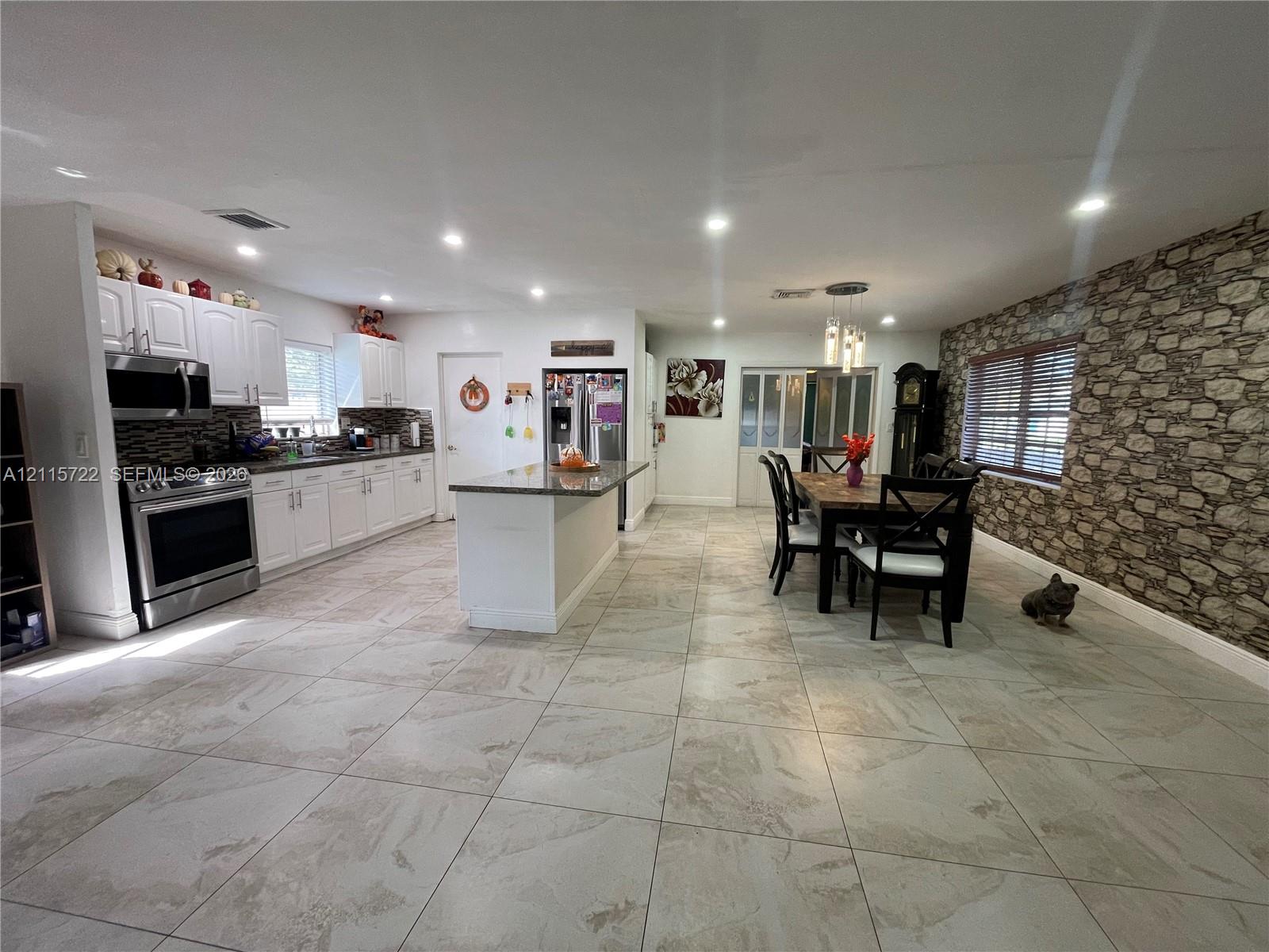 Kitchen featuring white cabinetry, stone-finish kitchen island, stainless steel appliances, large-format tile flooring, and stone-veneer accent wall