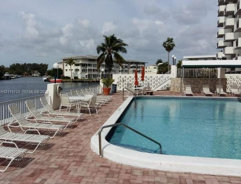 Waterfront swimming pool featuring a concrete deck with brick-style pavers and a metal perimeter railing