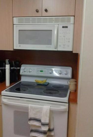 Built-in microwave oven, electric range with glass cooktop, and wooden cabinetry