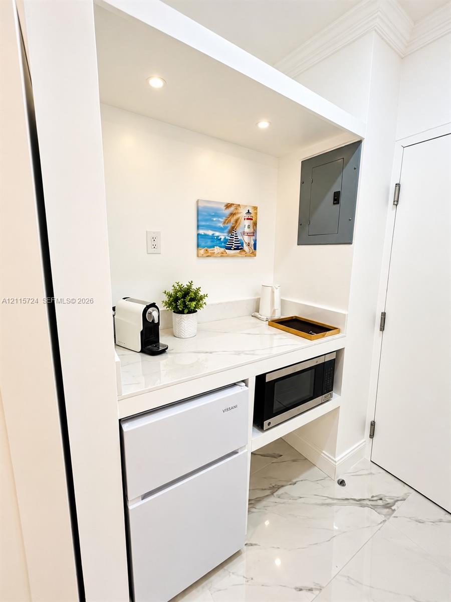 Built-in refreshment alcove featuring a stone-surface countertop, recessed lighting, integrated microwave, and white cabinetry