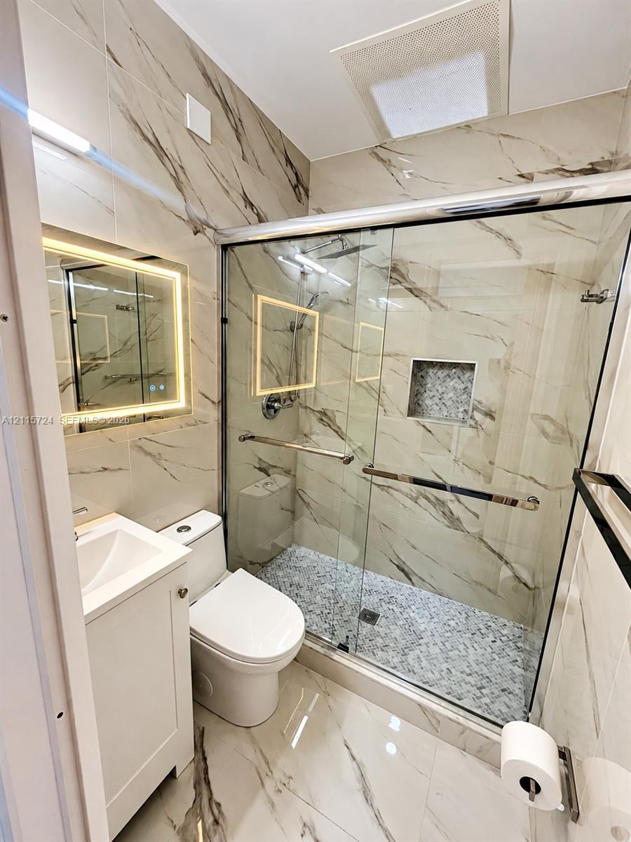 Walk-in shower with floor-to-ceiling vein-patterned tile, glass enclosure, built-in wall niche, and pebble-style stone shower flooring