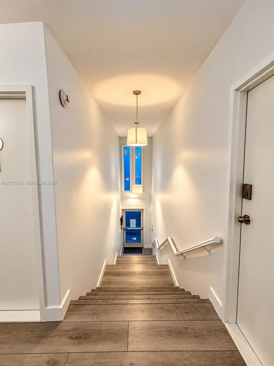 Staircase featuring wood-finish flooring, white walls, dual hanging pendant lights, and a white handrail