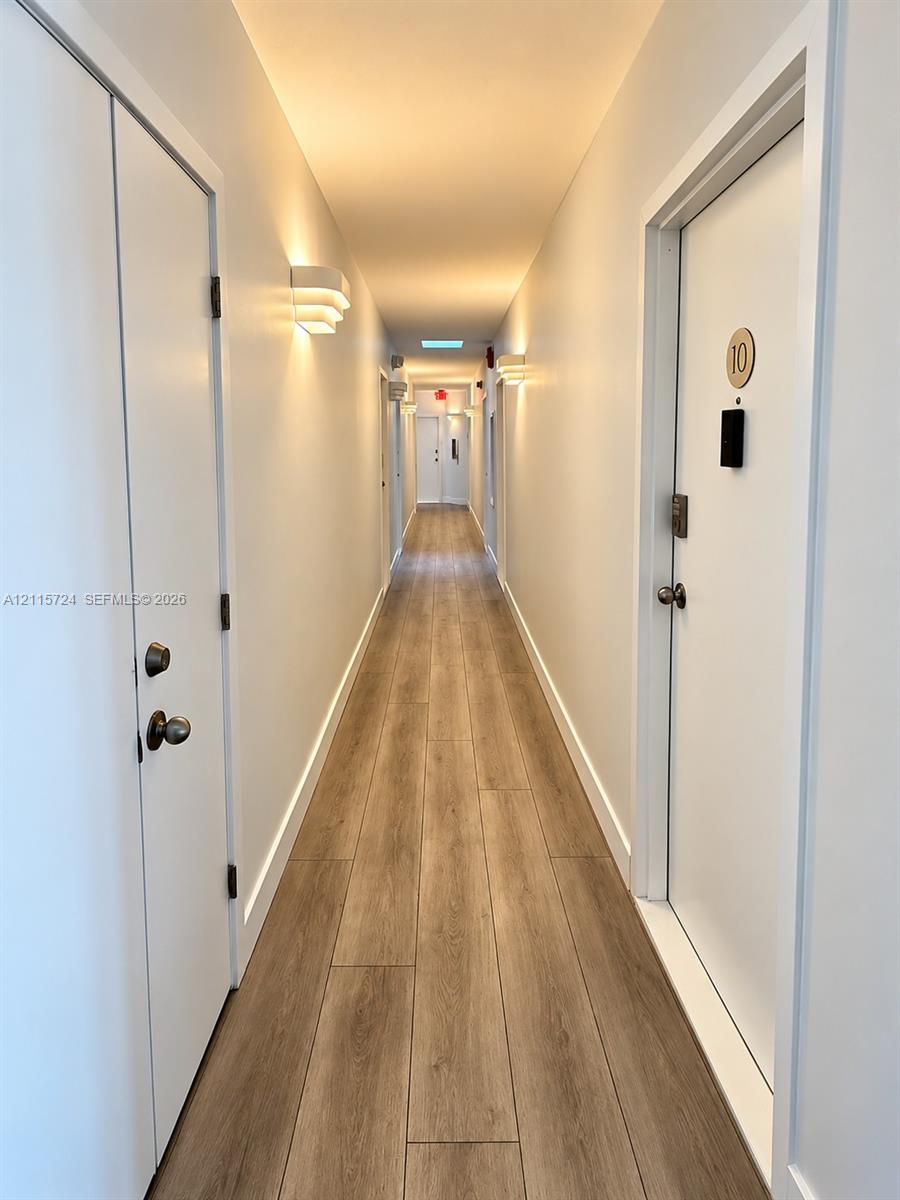 Hallway featuring wood-finish flooring, white doors with metallic hardware, and wall-mounted sconce lighting