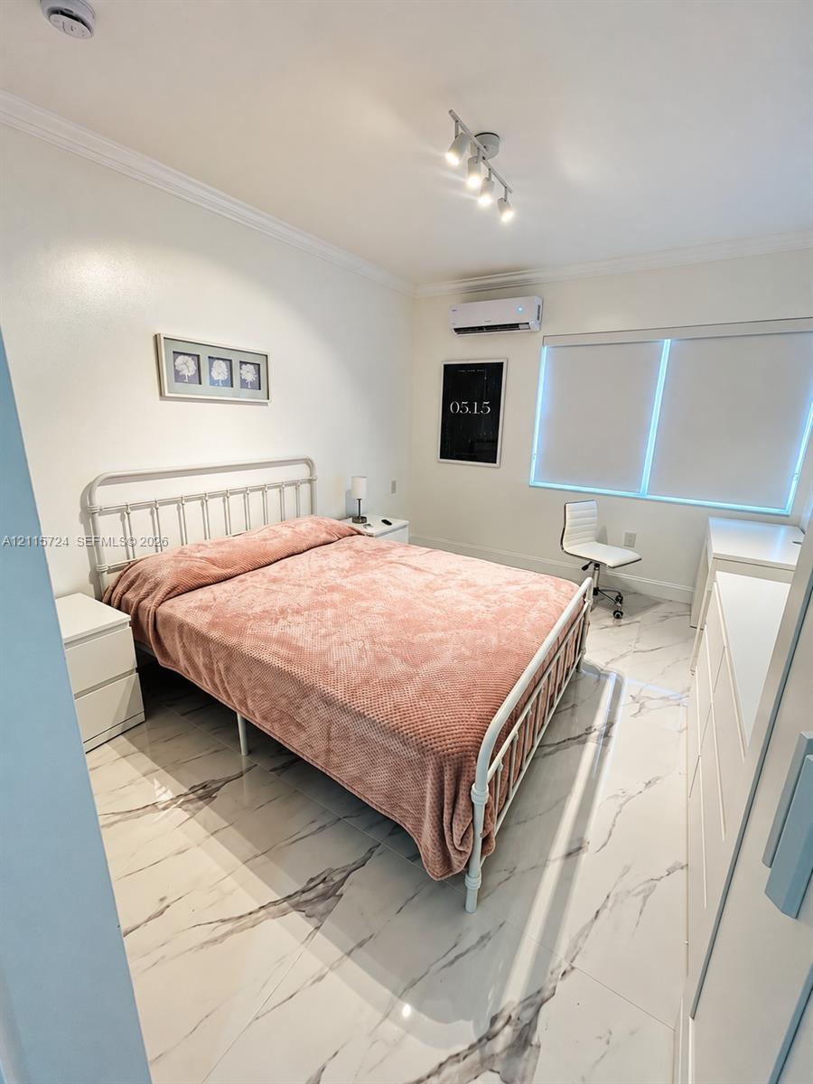 Large-format tile flooring featuring high-contrast veining, wall-mounted ductless climate control unit, multi-directional ceiling-mounted track lighting, and window with integrated roller shade Large-format tile flooring featuring high-contrast veining, wall-mounted ductless climate control unit, multi-directional ceiling-mounted track lighting, and window with integrated roller shade