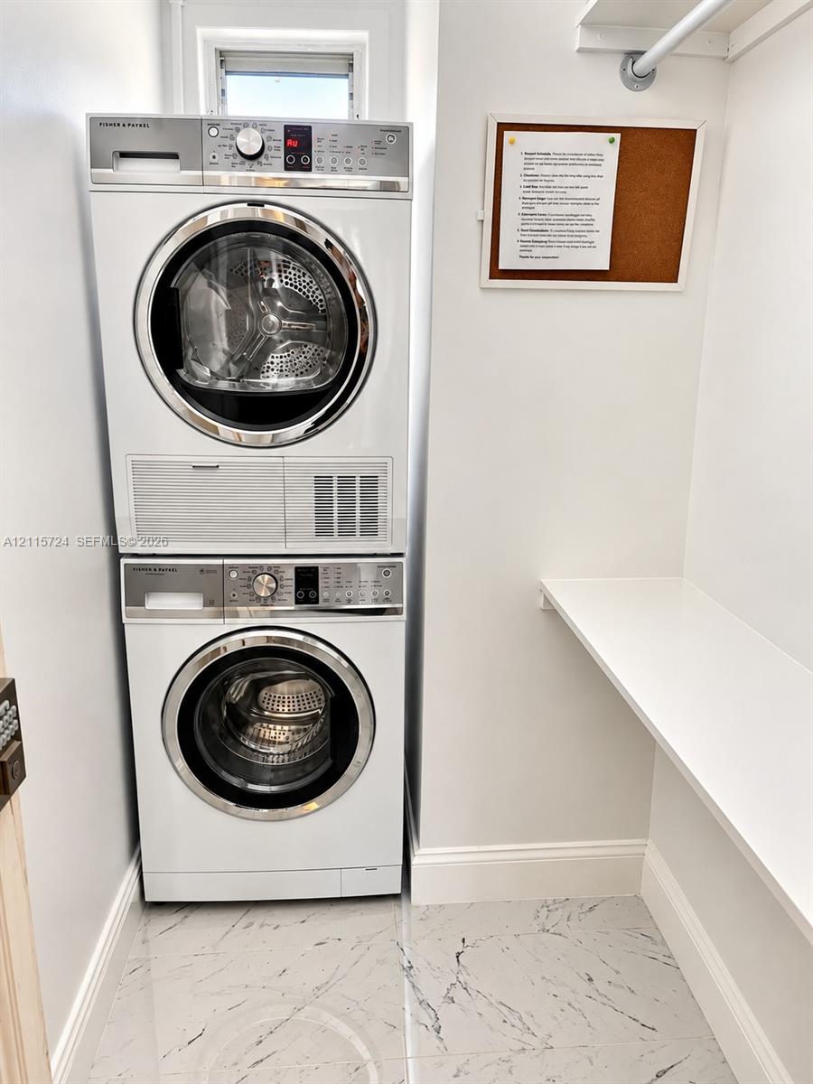Stacked white front-load washer and dryer, built-in wall shelf, overhead clothing rod, and polished stone-finish floor tiling