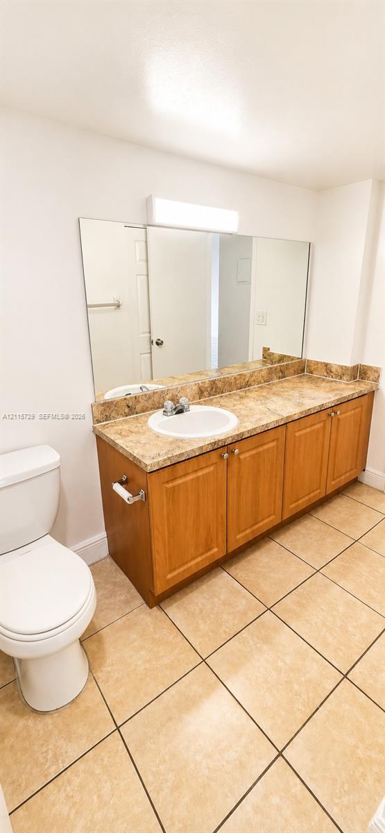 Vanity featuring a stone-pattern countertop, integrated round sink, wooden cabinetry, large wall-mounted mirror, and ceramic tile flooring