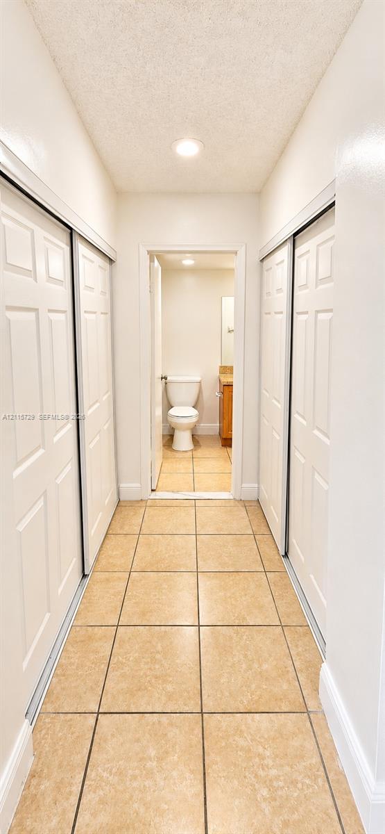 Hallway featuring ceramic tile flooring, recessed ceiling lighting, and dual sets of white paneled sliding closet doors